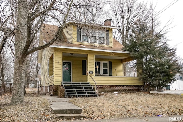 view of front facade with a shingled roof, covered porch, and a chimney