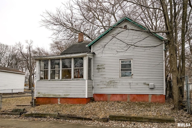 view of home's exterior featuring a sunroom, a chimney, and fence