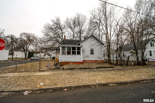 view of front of home with a sunroom, a chimney, fence, and a residential view