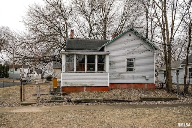 back of house with a gate, a chimney, fence, and a sunroom