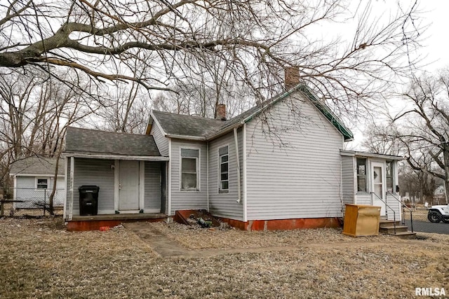 back of house featuring roof with shingles, fence, and a chimney