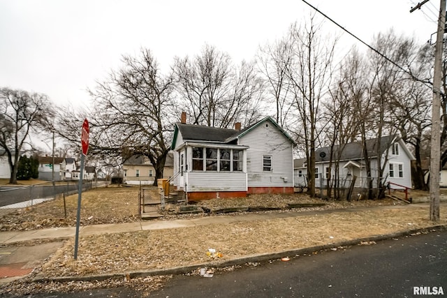 view of front of home with a sunroom, a fenced front yard, a chimney, and a residential view