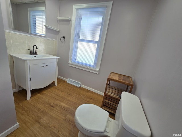 half bath featuring visible vents, toilet, wood finished floors, decorative backsplash, and baseboards