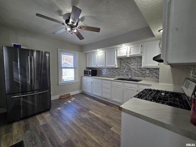 kitchen with a sink, backsplash, dark wood finished floors, appliances with stainless steel finishes, and white cabinets