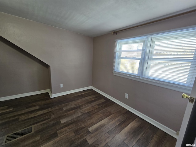 spare room featuring visible vents, baseboards, and dark wood-style floors