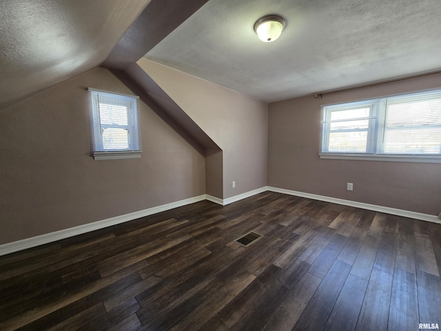 additional living space featuring baseboards, visible vents, dark wood-type flooring, vaulted ceiling, and a textured ceiling