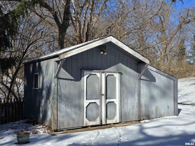 snow covered structure with an outdoor structure, a storage unit, and fence