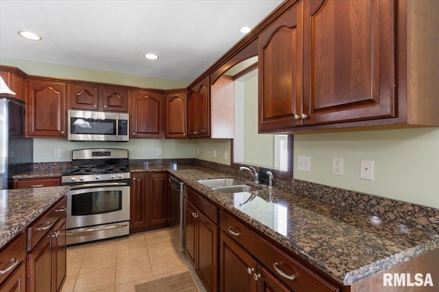 kitchen with appliances with stainless steel finishes, light tile patterned flooring, a sink, and dark stone countertops