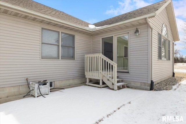 snow covered property entrance featuring a shingled roof