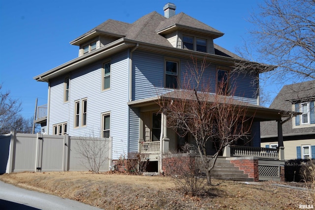 american foursquare style home with covered porch, roof with shingles, fence, and a gate