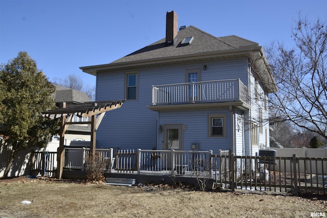 rear view of house with a balcony, a chimney, fence, a wooden deck, and a pergola