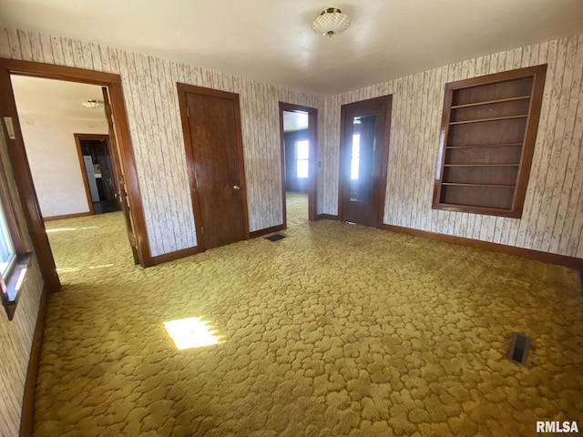 spare room featuring wallpapered walls, carpet, visible vents, and baseboards