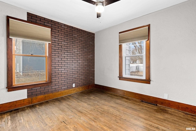 unfurnished room with baseboards, visible vents, brick wall, ceiling fan, and wood finished floors