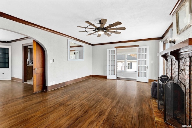 unfurnished living room with arched walkways, a fireplace, dark wood-style floors, and baseboards