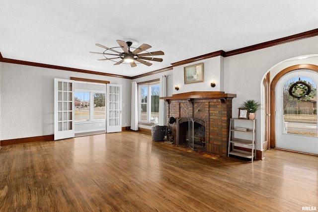 unfurnished living room featuring a brick fireplace, ceiling fan, baseboards, and wood finished floors