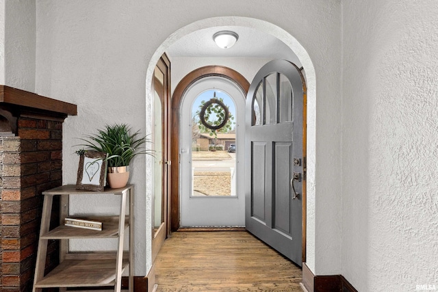 entryway featuring a textured ceiling, arched walkways, wood finished floors, and a textured wall