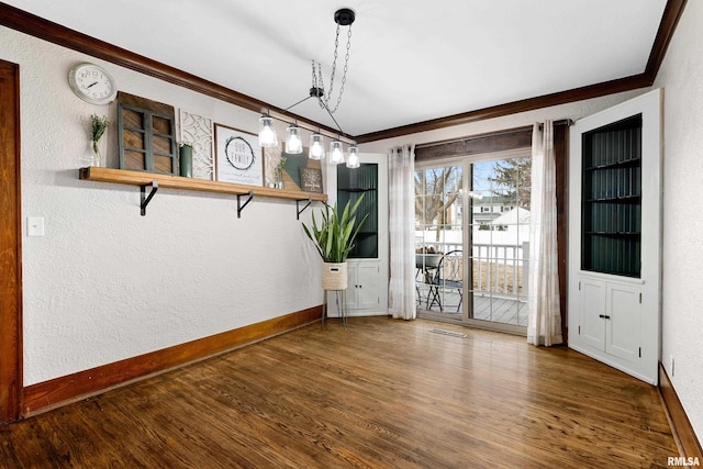 unfurnished dining area with ornamental molding, a textured wall, baseboards, and wood finished floors