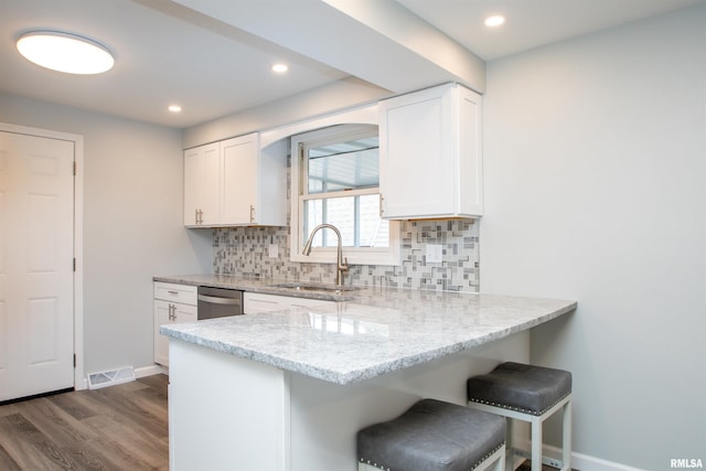 kitchen featuring white cabinets, a sink, light stone countertops, a kitchen bar, and stainless steel dishwasher