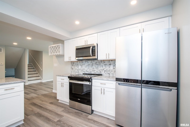 kitchen featuring light stone counters, stainless steel appliances, white cabinetry, light wood-style floors, and backsplash