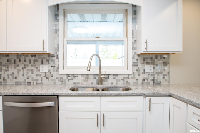 kitchen with a sink, light stone countertops, white cabinets, and stainless steel dishwasher