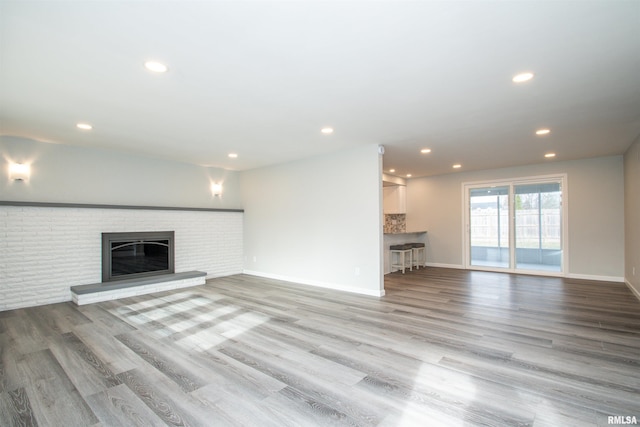 unfurnished living room with recessed lighting, a brick fireplace, light wood-style flooring, and baseboards