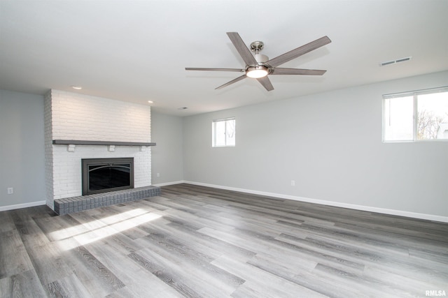 unfurnished living room with baseboards, visible vents, a ceiling fan, wood finished floors, and a fireplace