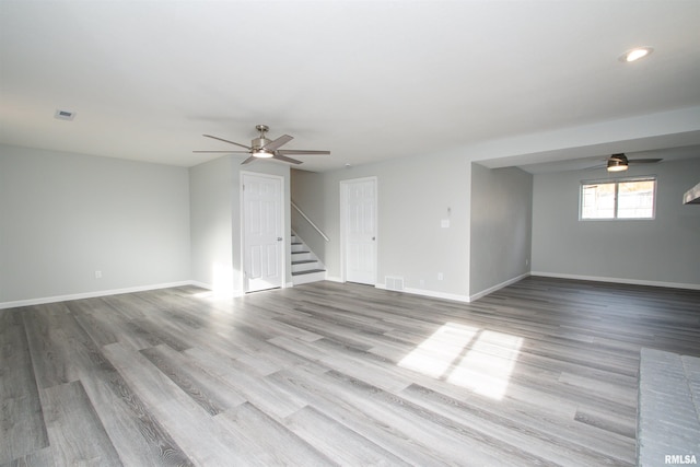 unfurnished room with visible vents, light wood-style floors, ceiling fan, baseboards, and stairs