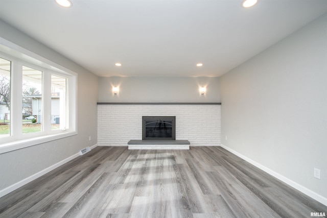 unfurnished living room featuring a brick fireplace, baseboards, wood finished floors, and recessed lighting