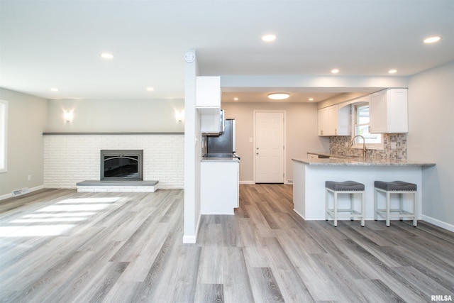 kitchen with a peninsula, white cabinets, a brick fireplace, tasteful backsplash, and a kitchen bar