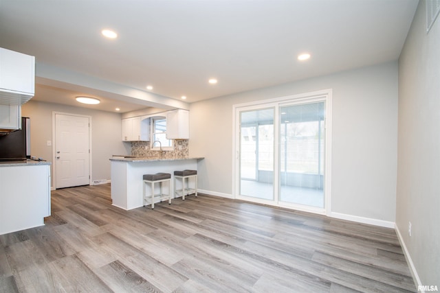 kitchen featuring decorative backsplash, a breakfast bar area, a peninsula, light countertops, and white cabinetry