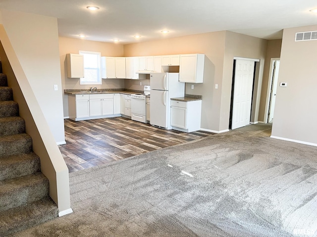 kitchen with white appliances, a sink, visible vents, white cabinetry, and dark colored carpet