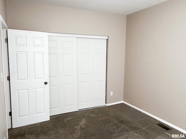 unfurnished bedroom with dark colored carpet, a closet, visible vents, and baseboards