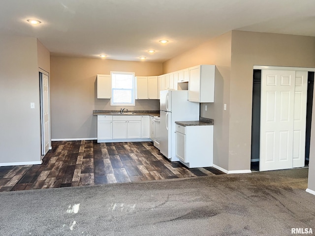 kitchen with baseboards, dark countertops, freestanding refrigerator, and white cabinets