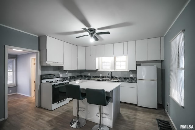 kitchen featuring a center island, white cabinetry, a sink, white appliances, and under cabinet range hood