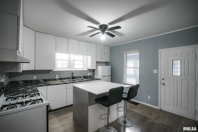 kitchen with dark countertops, gas stove, freestanding refrigerator, white cabinetry, and a kitchen island