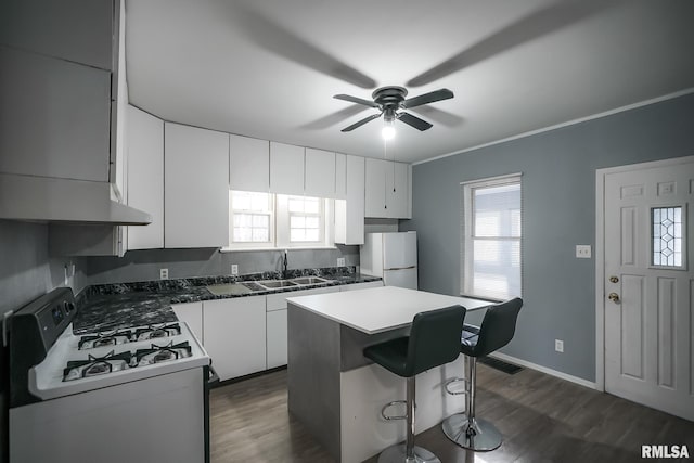 kitchen featuring dark countertops, white cabinetry, a kitchen island, a sink, and white appliances