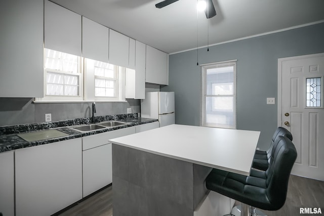 kitchen with dark countertops, white cabinets, a sink, and freestanding refrigerator