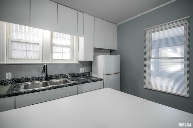 kitchen with dark stone counters, a sink, freestanding refrigerator, and white cabinets