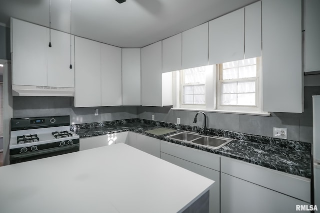 kitchen featuring under cabinet range hood, white cabinetry, range with gas stovetop, and a sink