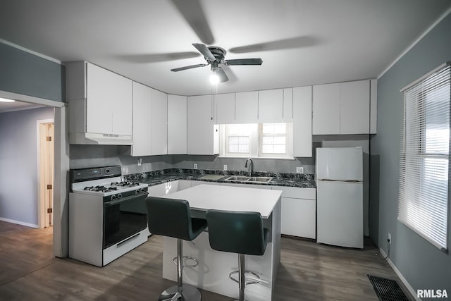 kitchen with white appliances, white cabinets, a center island, under cabinet range hood, and a sink