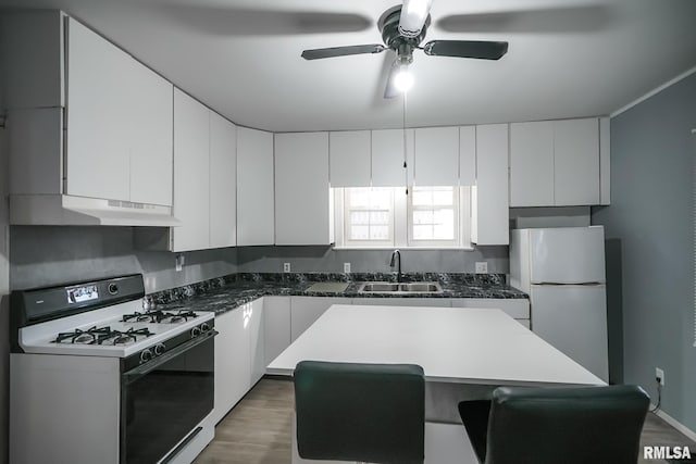 kitchen with white appliances, white cabinets, a center island, under cabinet range hood, and a sink