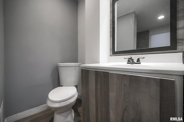 half bath with baseboards, vanity, toilet, and wood finished floors