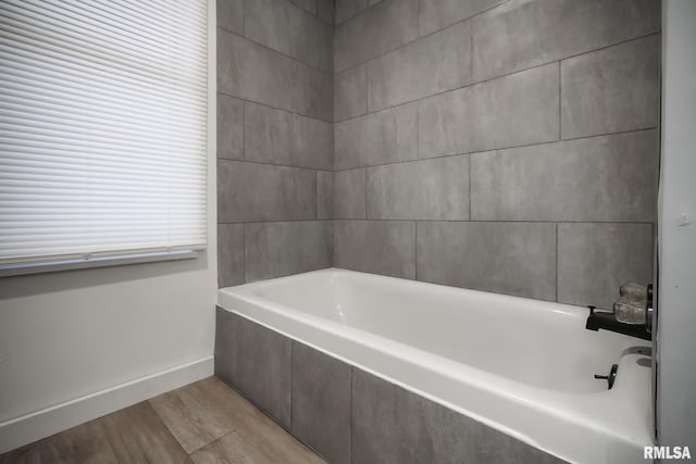 bathroom with a bathtub, baseboards, and wood finished floors