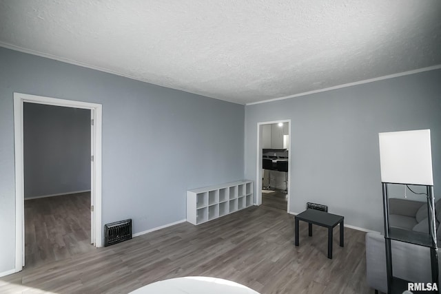 sitting room with a textured ceiling, baseboards, wood finished floors, and crown molding