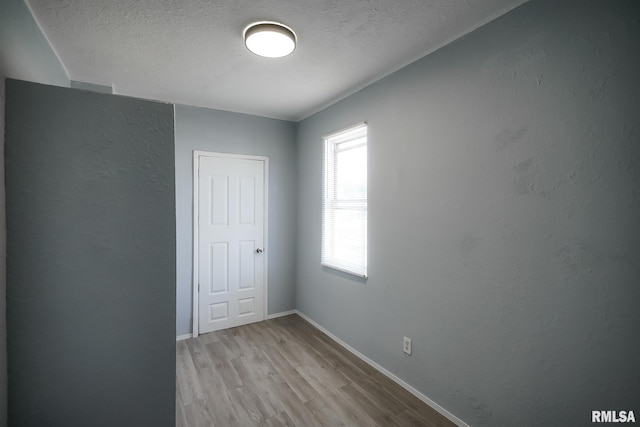 unfurnished room featuring light wood-style flooring, baseboards, and a textured ceiling