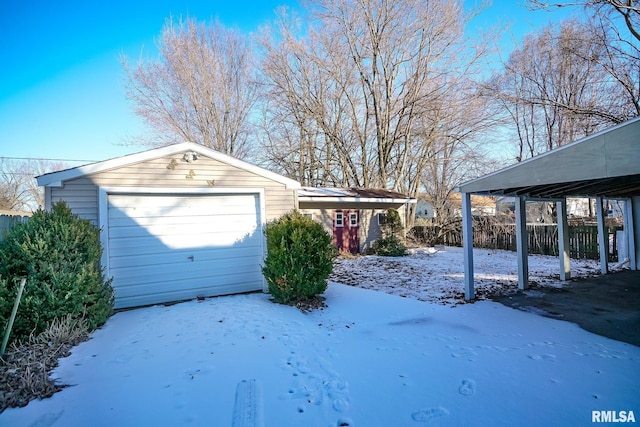 snow covered garage featuring a garage and fence