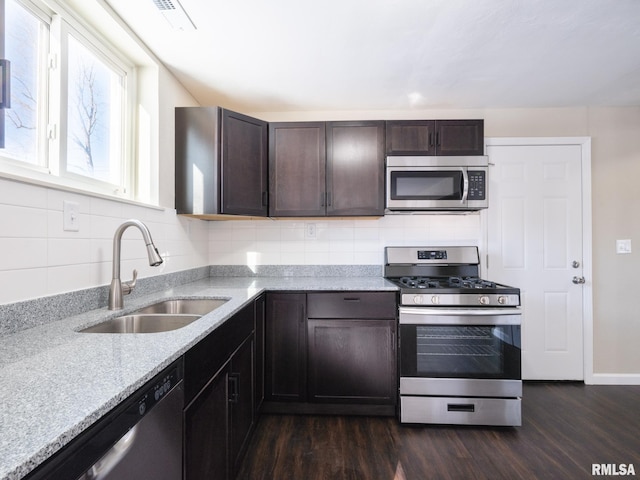 kitchen featuring light stone counters, stainless steel appliances, dark wood-style flooring, a sink, and dark brown cabinets