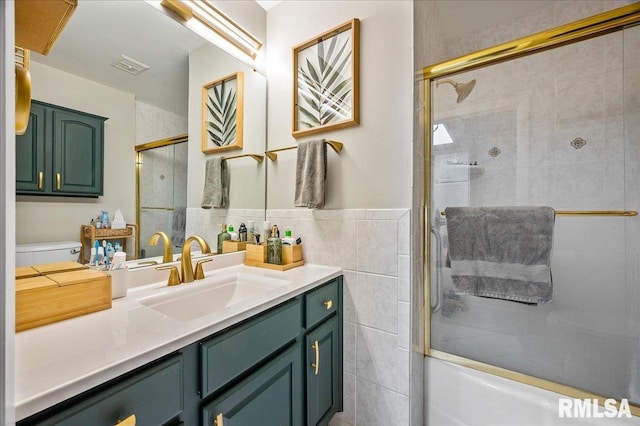 bathroom with visible vents, bath / shower combo with glass door, toilet, vanity, and tile walls