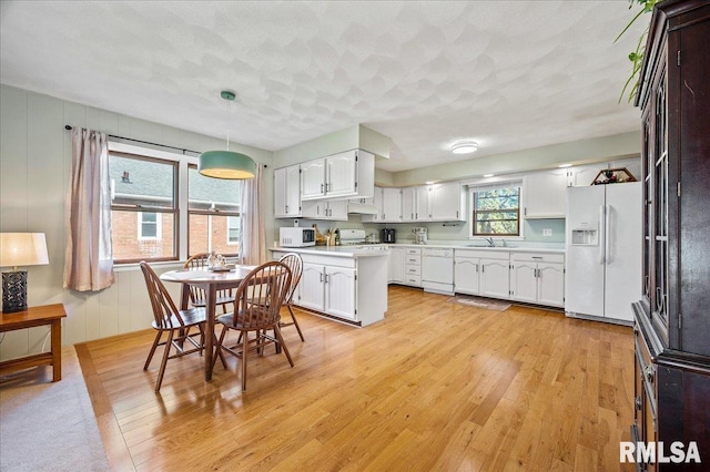 kitchen with white appliances, white cabinets, light countertops, pendant lighting, and a sink