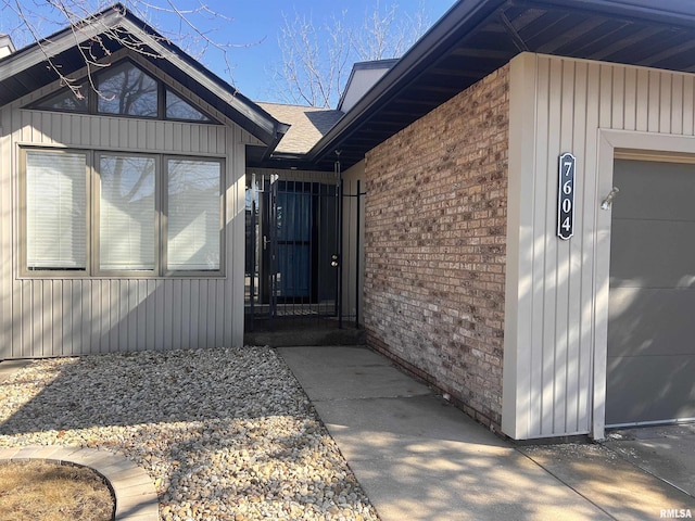 property entrance with a garage, brick siding, and roof with shingles